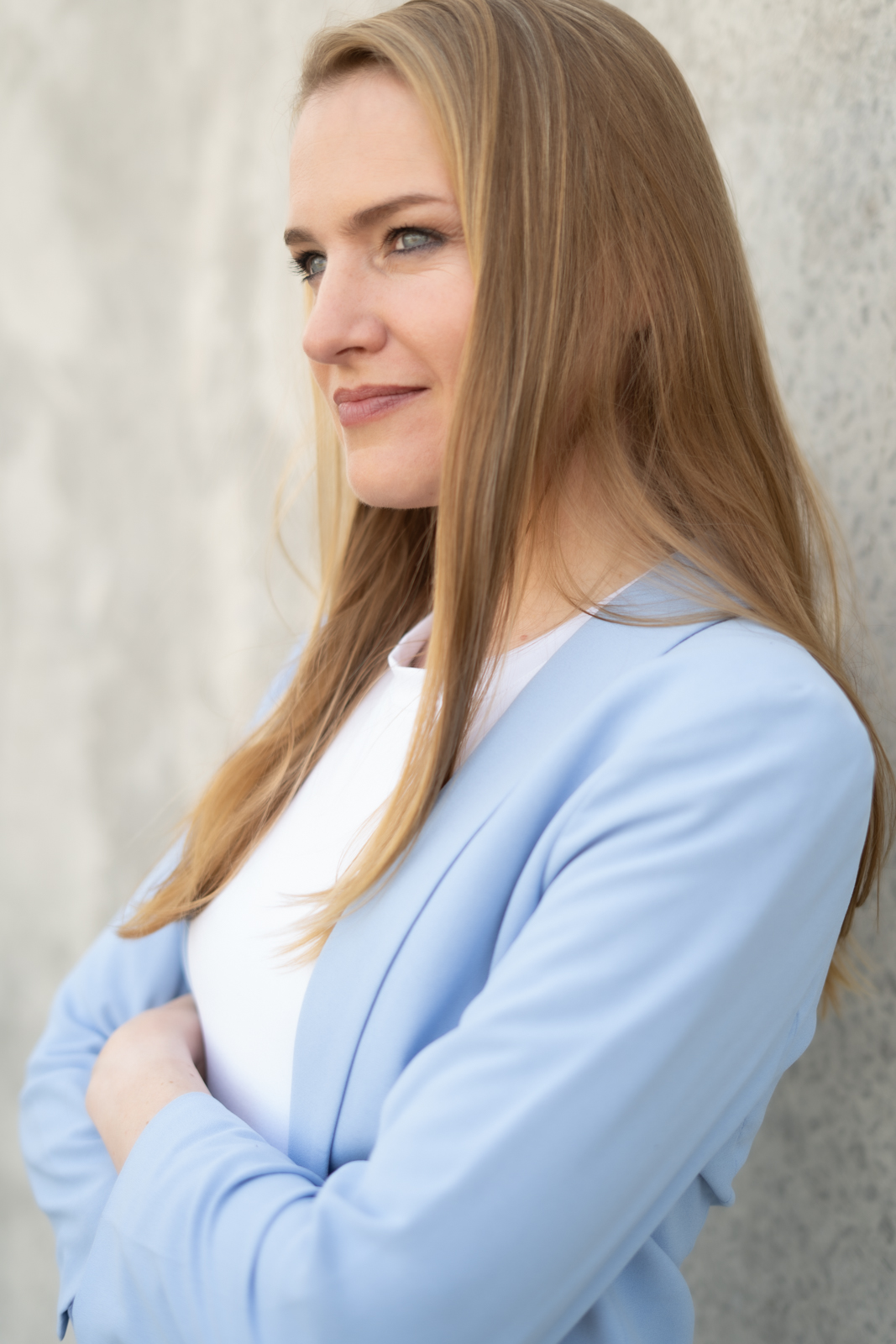 Ramona Isabel Hertel im hellblauen Blazer vor einer Betonwand